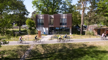 Naturpark-Haus Das Naturpark-Haus mit seiner modernen Glasfassade ist von Radfahrern auf einer Allee umgeben.