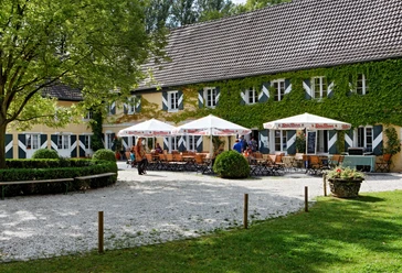 Gastronomie der Wasserburg Haus Graven in Langenfeld Sonniger Außenbereich der Wasserburg Haus Graven mit einladenden Sitzgelegenheiten und üppiger Begrünung.