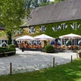 Gastronomie der Wasserburg Haus Graven in Langenfeld Sonniger Außenbereich der Wasserburg Haus Graven mit einladenden Sitzgelegenheiten und üppiger Begrünung.