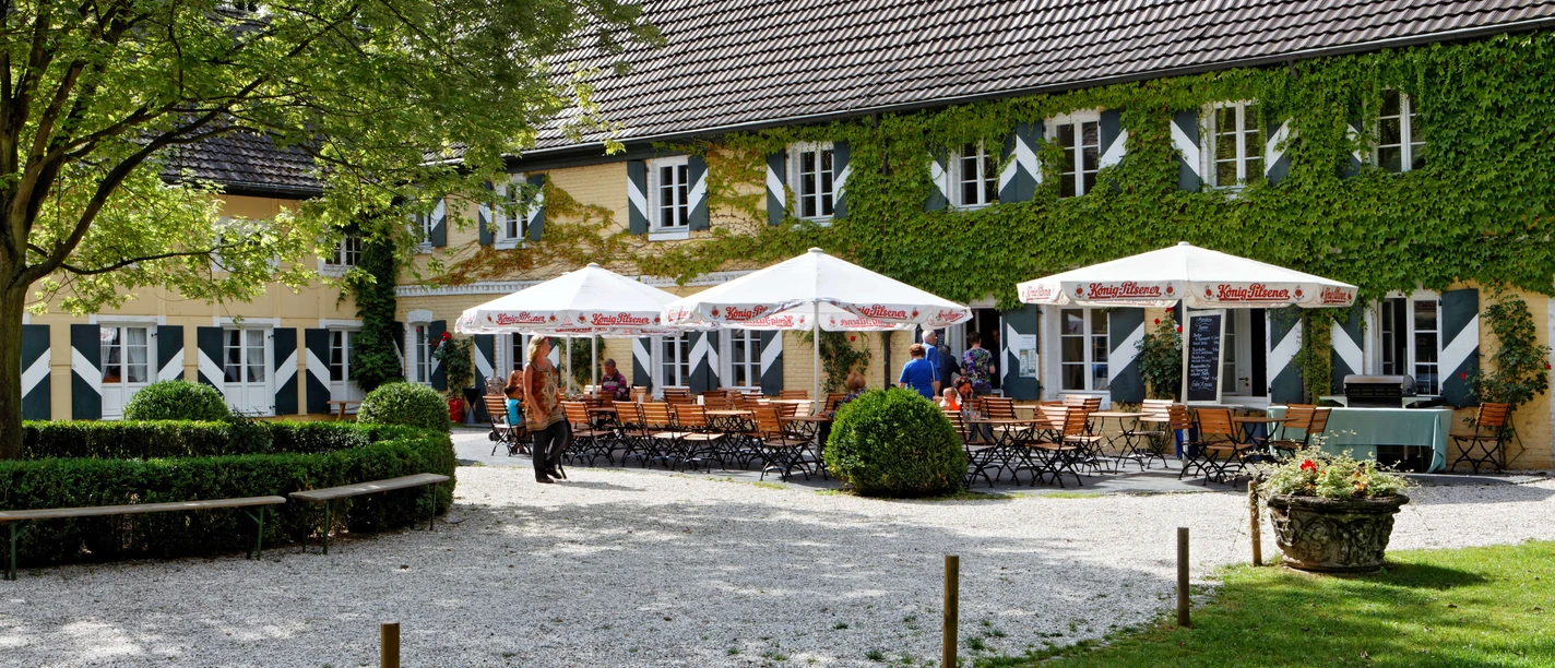 Gastronomie der Wasserburg Haus Graven in Langenfeld Sonniger Außenbereich der Wasserburg Haus Graven mit einladenden Sitzgelegenheiten und üppiger Begrünung.