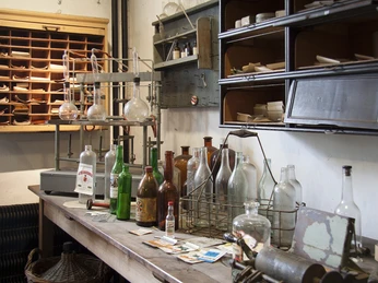 Labor der Kornbrennerei im Wilhelm-Fabry-Museum in Hilden In einem historischen Labor stehen alte Glasflaschen und Retorten auf einem Holztisch im Museum.