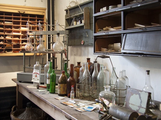 Labor der Kornbrennerei im Wilhelm-Fabry-Museum in Hilden In einem historischen Labor stehen alte Glasflaschen und Retorten auf einem Holztisch im Museum.