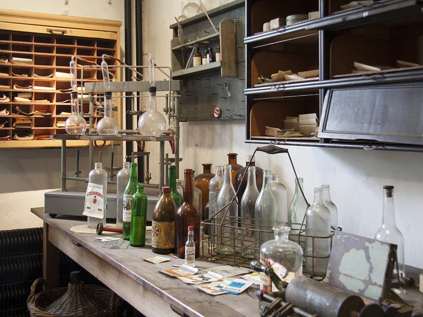Labor der Kornbrennerei im Wilhelm-Fabry-Museum in Hilden In einem historischen Labor stehen alte Glasflaschen und Retorten auf einem Holztisch im Museum.