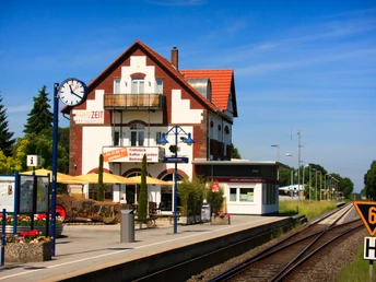 Bahnhof Oerlinghausen in Asemissen_IMG_7058.jpg Bahnhof mit zwei Gleisen, Fachwerkhaus, blauer Himmel, Uhr und Hinweisschilder auf dem Bahnsteig.