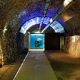 Zeittunnel Wülfrath Beleuchteter Tunnel mit gewölbtem Steinhaus und einem leuchtenden Plakat mit einem Schädelmotiv.