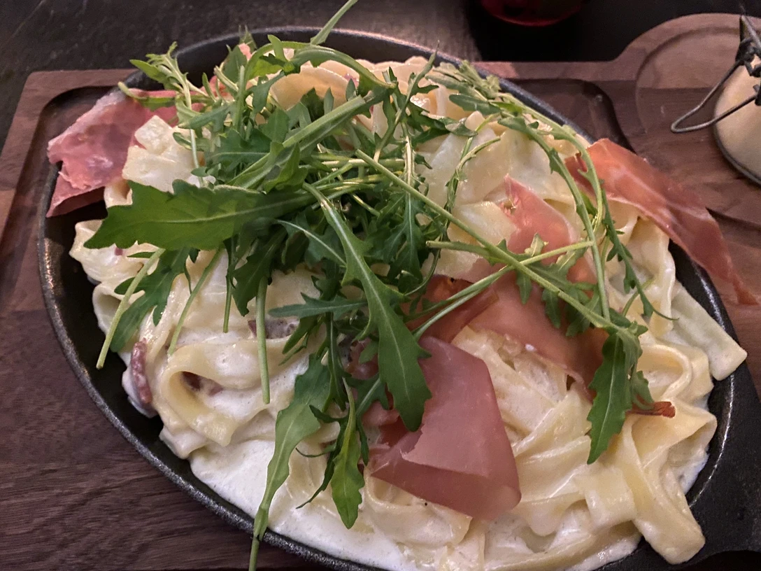 Nudelgericht Ein Teller mit Tagliatelle in cremiger Soße, garniert mit Rucola und Schinken auf einem Holztisch.
