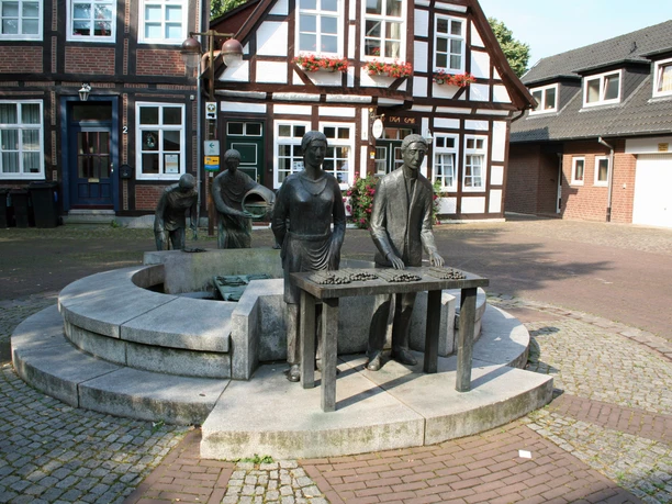 Bronze statue of a man and a woman with asparagus, fountain in front, half-timbered houses in the background.