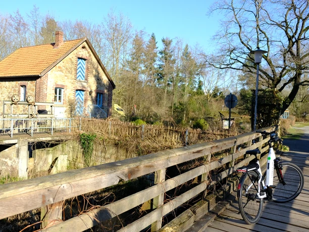 Heerser Mühle Bad Salzuflen.JPG Fachwerkhaus mit Backsteinmauern, neben einem Holzzaun, im ländlichen Umfeld mit Fahrradständer.