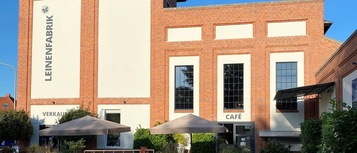 Brick building with gray façade, shaded terrace, salesroom and café under parasols.
