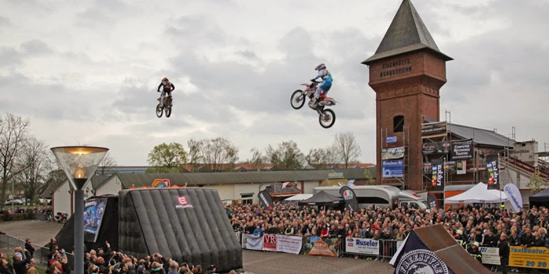 Stuntshow in Augustfehn Motorradstuntfahrer springen durch die Luft vor einer großen Menschenmenge am Eisenhüttenplatz.