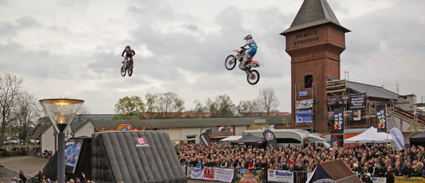 Stuntshow in Augustfehn Motorradstuntfahrer springen durch die Luft vor einer großen Menschenmenge am Eisenhüttenplatz.