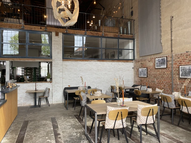 LEINENFABRIK Innenansicht I Ein helles, modernes Café mit hohen Decken, Holzmöbeln und großen Glasfenstern.
