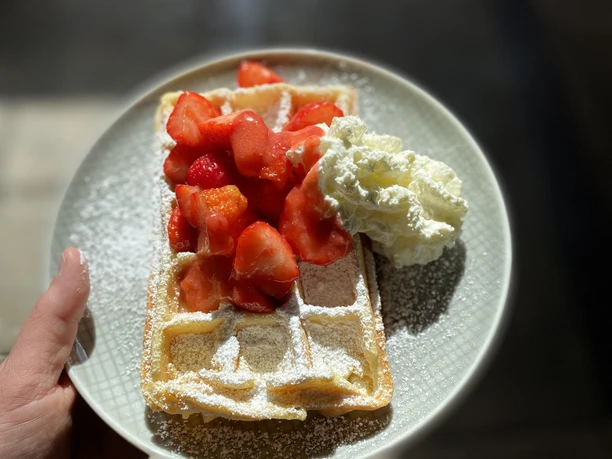 Fresh waffle sprinkled with powdered sugar, served with sliced strawberries and a dollop of cream.