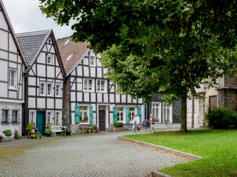 Kirchplatz in der Wülfrather Altstadt Historischer Kirchplatz in Wülfrath mit Fachwerkhäusern und Kopfsteinpflaster, von Bäumen umgeben.