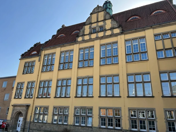 Historisches Gebäude mit gelber Fassade, vielen Fenstern und markanter Dachform bei blauem Himmel.