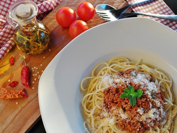 bottrop+restaurant-im-maschinenhaus+bild02.jpg Spaghetti mit Bolognese, bestreut mit Parmesan, neben Gewürzöl, Tomaten und Chili auf Holztisch.