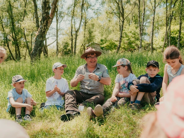 Ranger sitzt mit Kindern im Gras