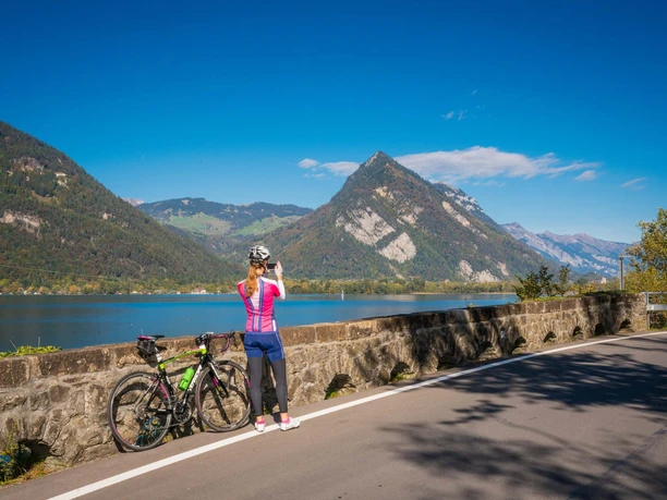 A female cyclist with a road bike is taking a photo towards Interlaken with the Harder