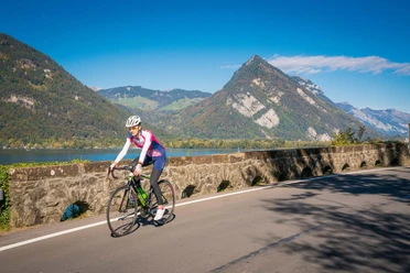 Une cycliste sur un vélo de route entre Interlaken et Spiez, en arrière-plan le lac de Thoune ainsi que le Harder