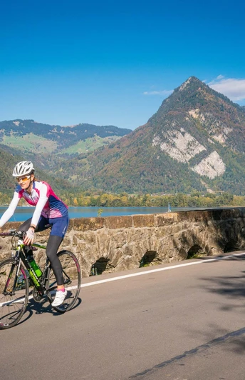 Eine Bikerin auf einem Rennrad unterwegs zwischen Interlaken und Spiez, im Hintergrund der Thunersee sowie der Harder
