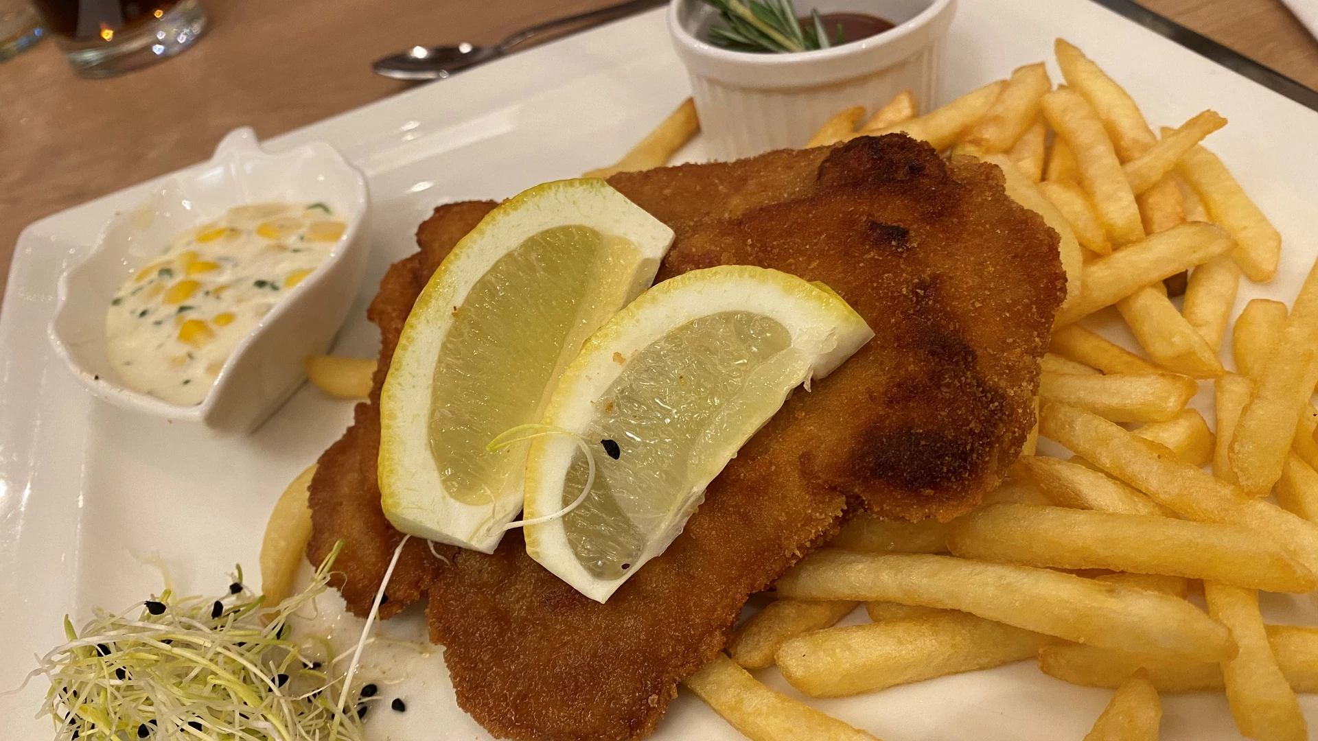 Two lemon slices on a crispy schnitzel, served with chips and herb dip, decorated with sprouts.