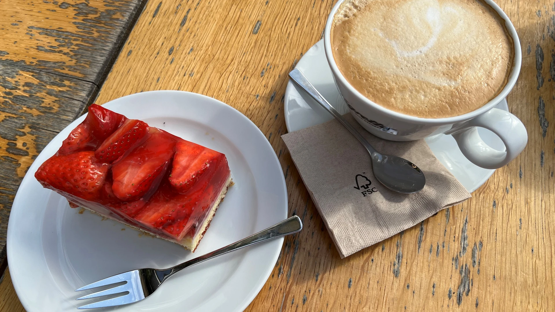 Coffee cup with latte art and piece of strawberry cake on wooden table, ready to enjoy.
