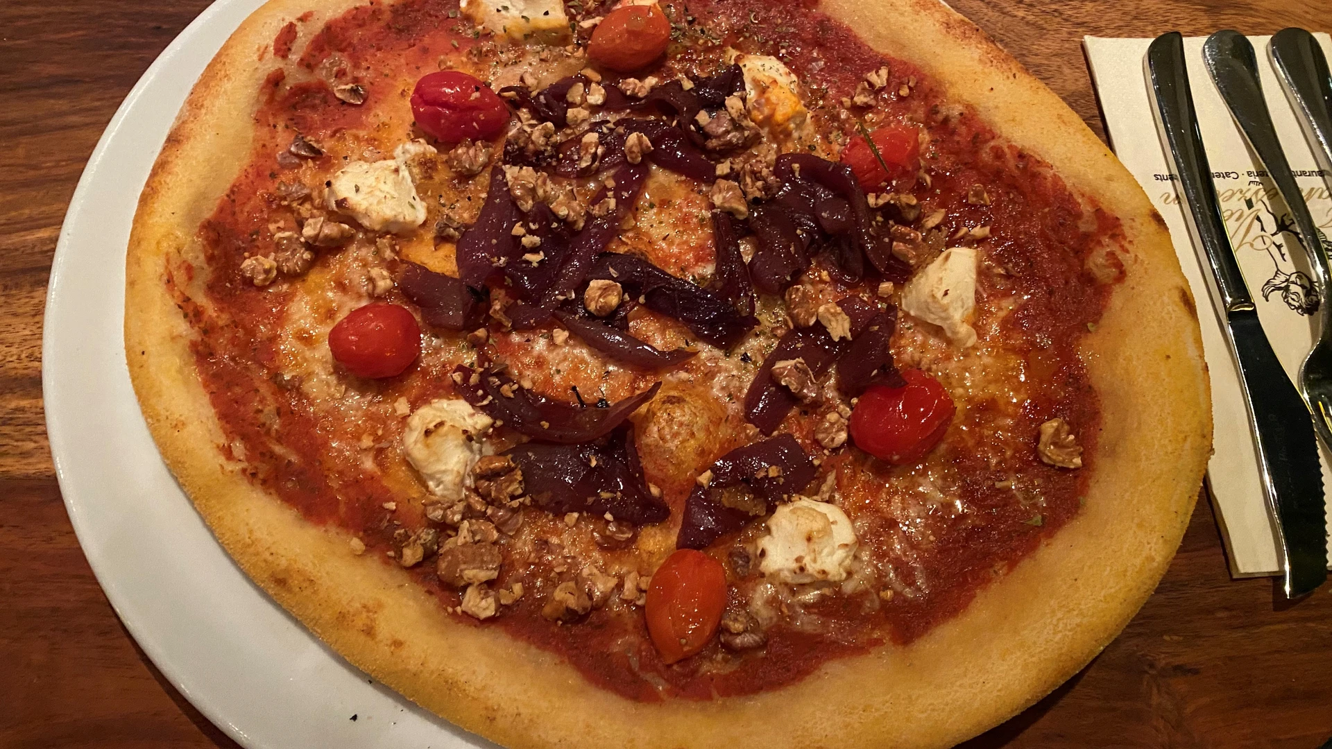 A crispy pizza with red cherry tomatoes, purple onion strips and pieces of light cheese.