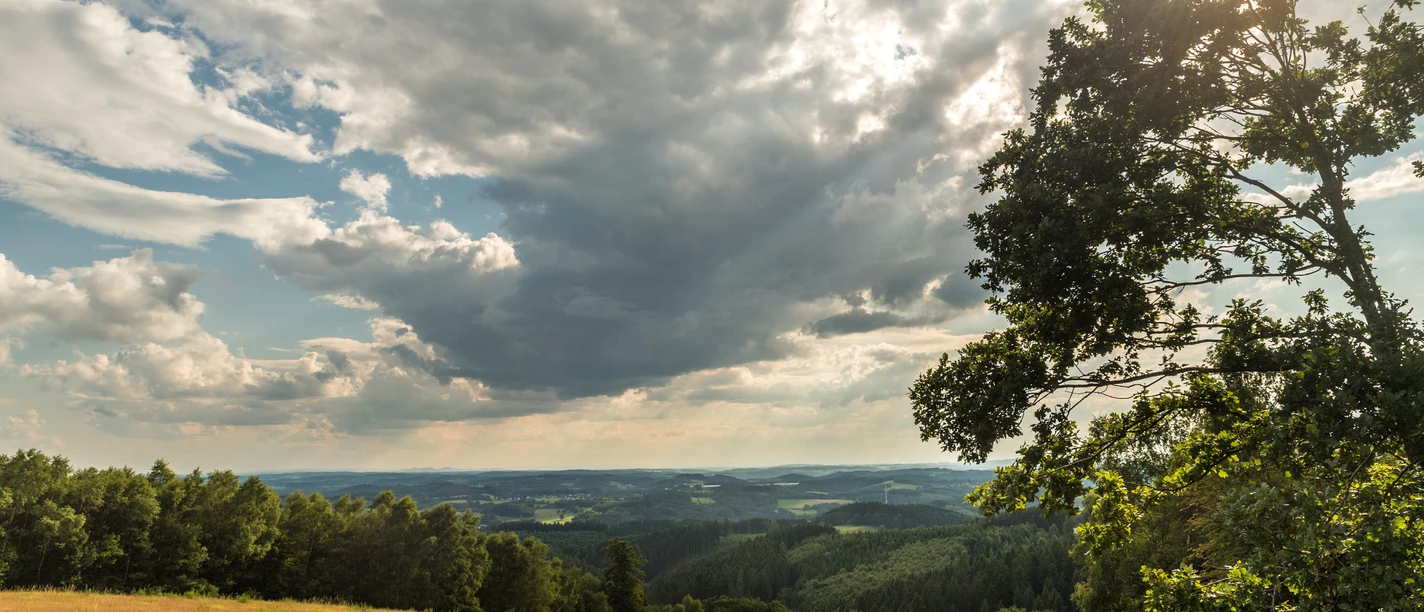 Reichshof Blockhaus Prachtig heuvelachtig landschap met bloeiende weiden, bossen en een dramatische, bewolkte hemel in de zon.