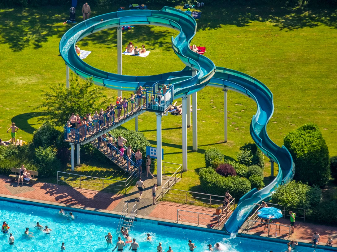 Heiligenhaus'taki Heljensbad Yeşil çimlerle çevrili, kavisli mavi su kaydırağı bulunan açık havuz.