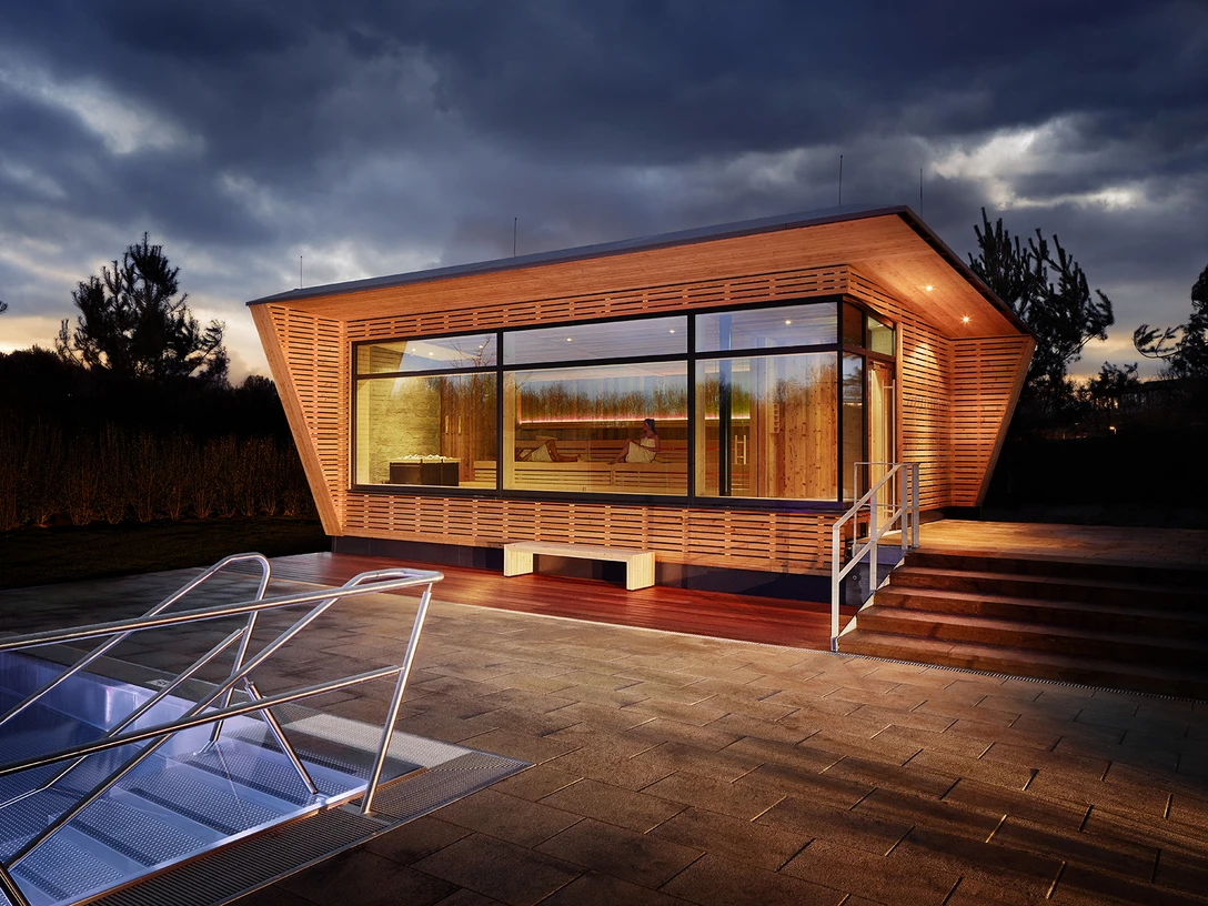 Mona Mare à Monheim am Rhein Bâtiment moderne avec de grandes façades vitrées, entouré d'escaliers éclairés et de dalles de pavage.