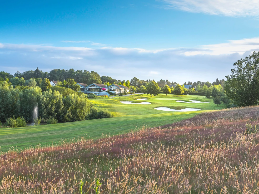 Heiligenhaus'taki Hösel Golf Kulübü Ağaçlarla çevrili, arka planda bir kulüp binası bulunan, bakımlı yeşilliklere ve kum tuzaklarına sahip golf sahası.