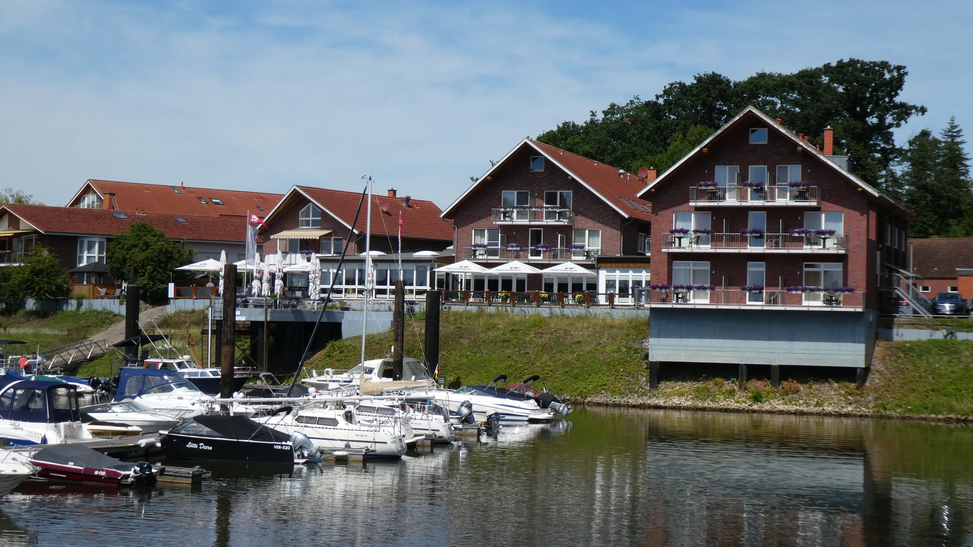 A hotel-restaurant with red brick walls on the shore, surrounded by boats on the calm water.