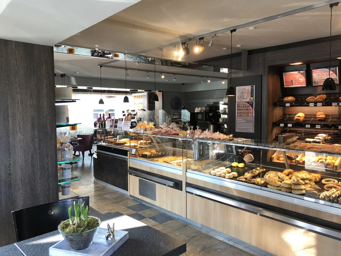 Droste Cafe, Ratingen'de pastane ve catering Modern iç mekanlar ve oturma alanlarıyla çevrili, tezgahları pasta ve keklerle dolu aydınlık bir kafe.