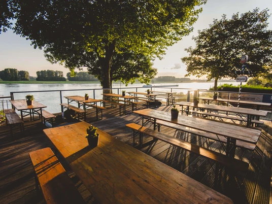 Haus Rheinblick Ott in Monheim Sunset over the Rhine with empty beer garden tables on a wooden terrace in the foreground.
