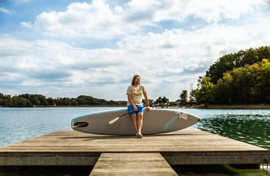 Stand-up paddling A man sits on a stand-up paddleboard on a wooden jetty on an idyllic lakeshore in sunshine.