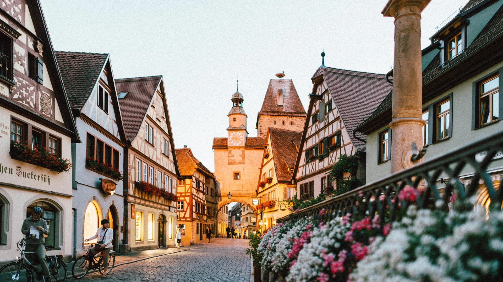 Historische Gasse mit Fachwerkhäusern, Blüten und einem Turm im Abendlicht