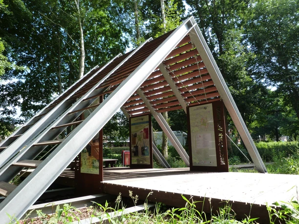 Veenloopcentrum Weiteveen Modernes Informationspavillon mit Schautafeln und Metallbalken im Grünen unter hohen Bäumen.