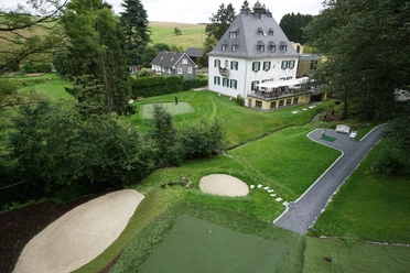 Short Game Area A historic villa surrounded by green countryside and a well-maintained golf course with sand bunkers.
