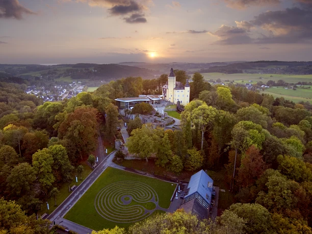 Kasteel Homburg Luchtfoto van kasteel Altena in Noordrijn-Westfalen, omgeven door een weelderig boslandschap bij zonsondergang.