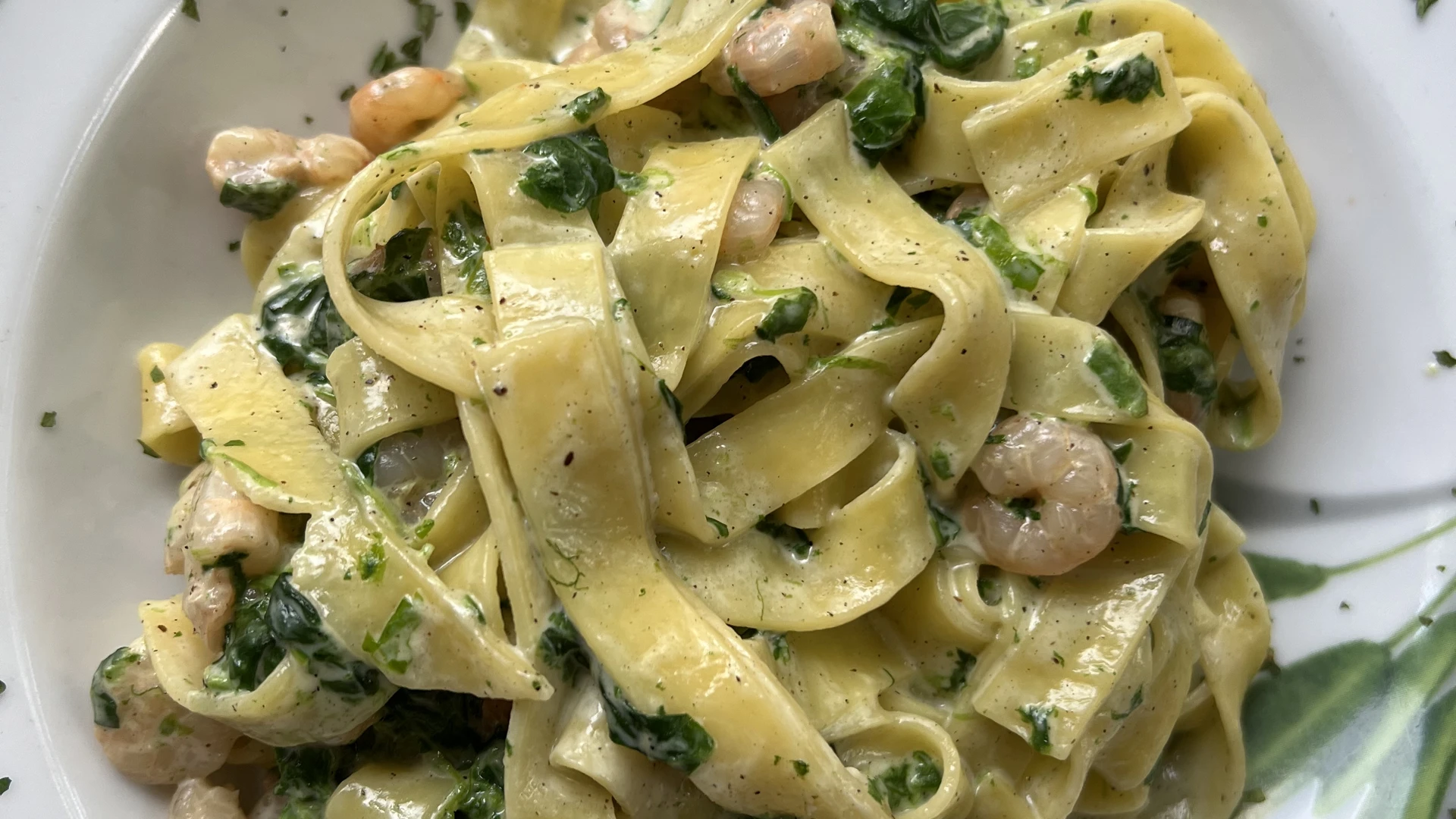 Ribbon noodles with prawns, fresh herbs and spinach leaves served on a white plate.