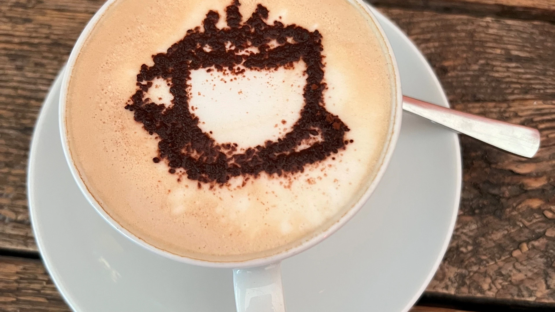 A cappuccino cup with a cocoa powder motif on frothy milk, served on a wooden table.