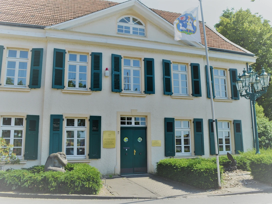 Monheim am Rhein'daki Deusser Evi Yeşil-beyaz panjurlu, mavi giriş kapılı ve Kuzey Ren-Vestfalya bayrağına sahip tarihi bina.