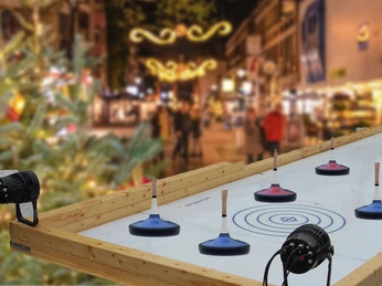 Curling al mercatino di Natale Una pista di curling illuminata in un vivace mercatino di Natale con luci.