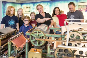 Familie bij de papiermachine in het laboratorium Een gezin bekijkt onder begeleiding van een medewerker een historische papiermachine in een museum.