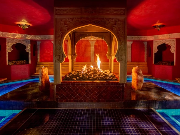 Mediterranean An oriental spa with a fire pit, surrounded by blue pools of water, bathed in warm light.