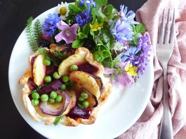 Wilde kruidensalade met zure Hartige taart met aardappelen, erwten en rode uien, gegarneerd met eetbare bloemen en kruiden.