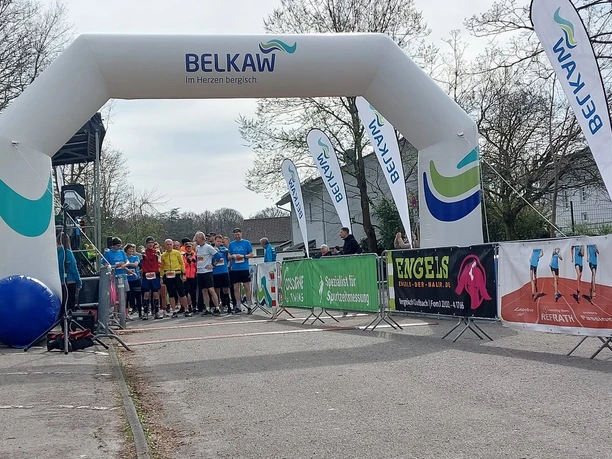 50e marathon van Königsforst Een groep hardlopers wacht bij de start van een sportevenement onder een grote witte boog in de openlucht.