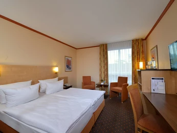 Pokoje hotelowe w Sure Hotel by Best Western Hilden-Düsseldorf Jasny pokój hotelowy z dużym podwójnym łóżkiem, dwoma krzesłami, stołem i biurkiem z telewizorem.