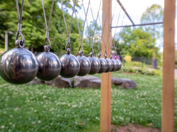 Spa-tuinen in Reichshof-Eckenhagen: Zintuiglijke elementen Negen symmetrisch opgehangen metalen bollen in de vorm van een Newton-wieg, buiten in een groene omgeving.