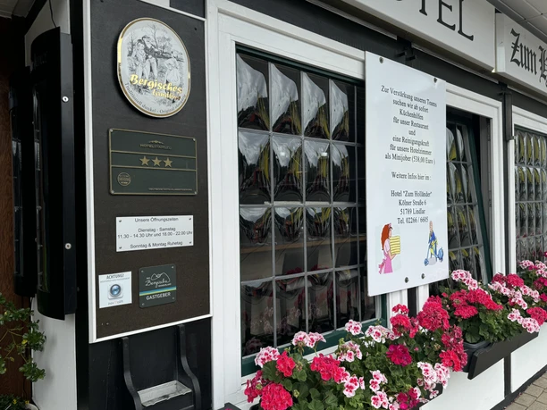 Hotel-Restaurant Zum Holländer - Buitenaanzicht De voorkant van een hotel met uithangborden en bloeiende geraniums voor een raam.